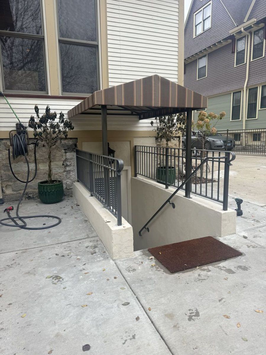 Exterior basement entrance with awning, railing, and steps