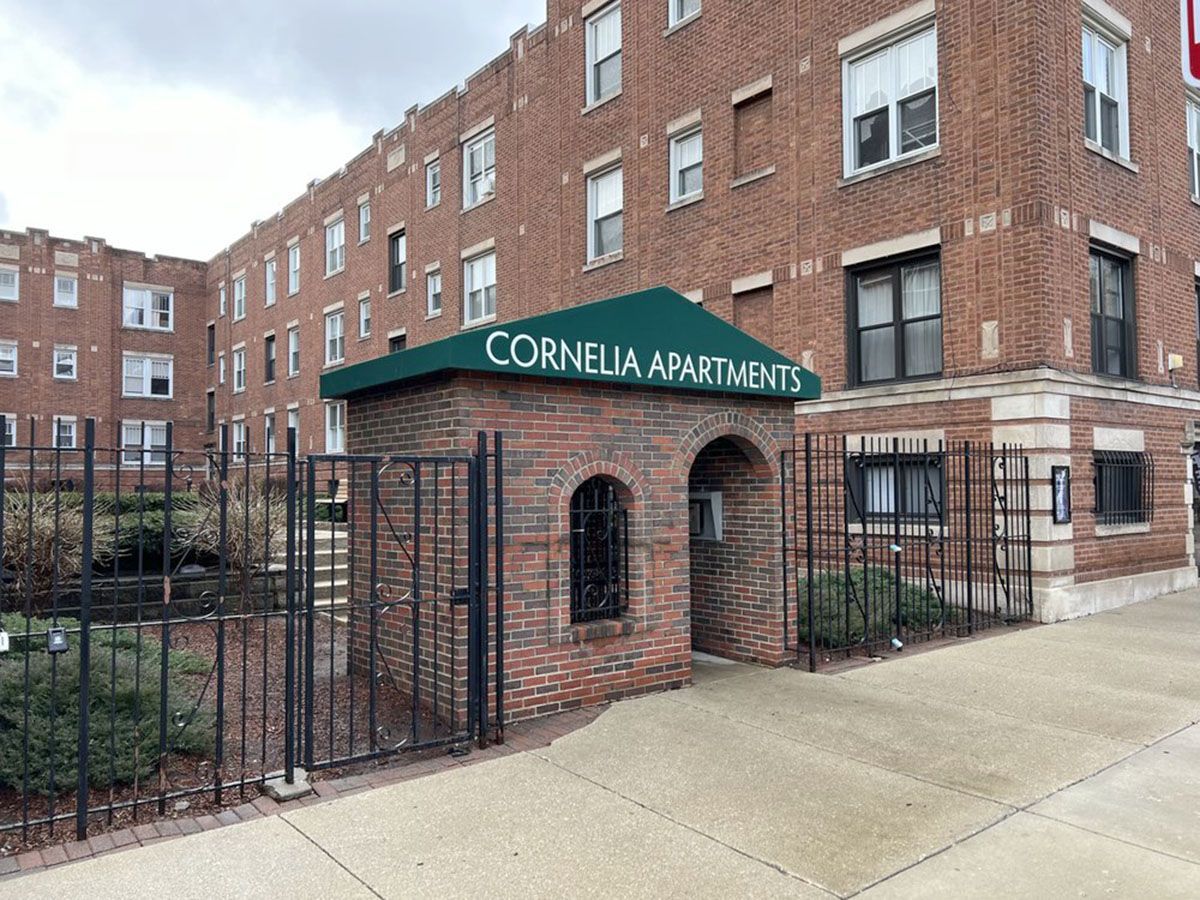 An apartment building entrance with brick facade and awning, black iron gate, and sidewalk