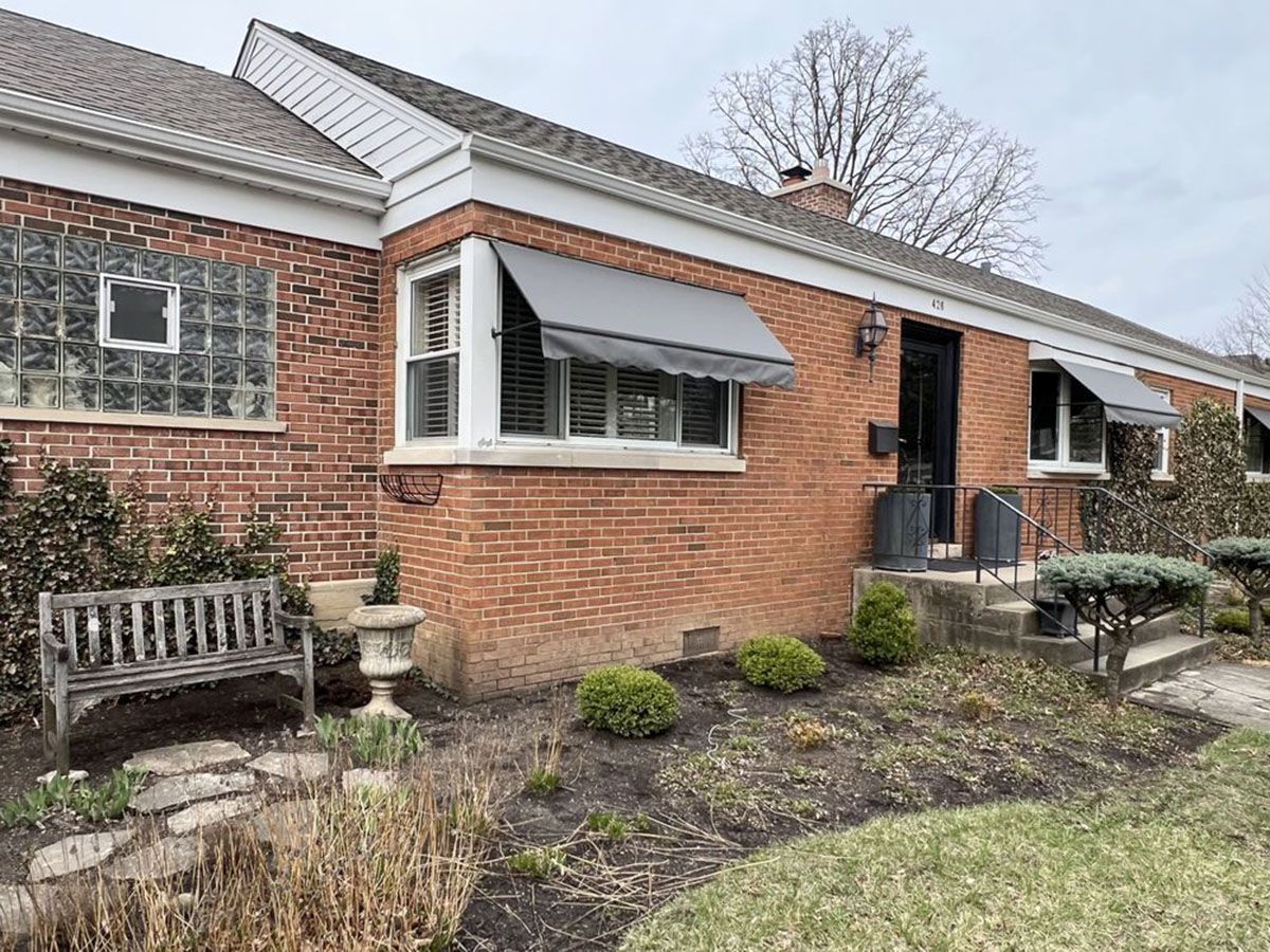 Brick house with gray awnings, shutters, glass block window, and front yard landscaping