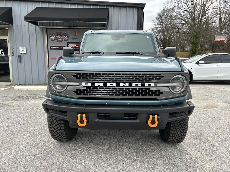 The front of a ford bronco is parked in front of a building.