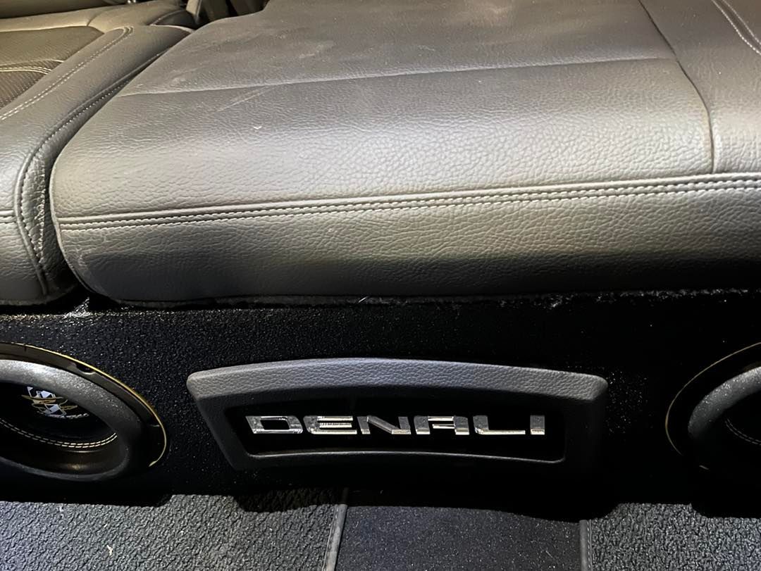 A denali subwoofer is sitting under a seat in a car.