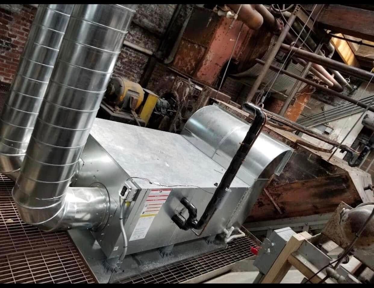 Industrial HVAC unit with ductwork in a metallic, brick-lined setting.