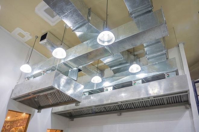 Restaurant ceiling with ductwork, exhaust hoods, and pendant lights.