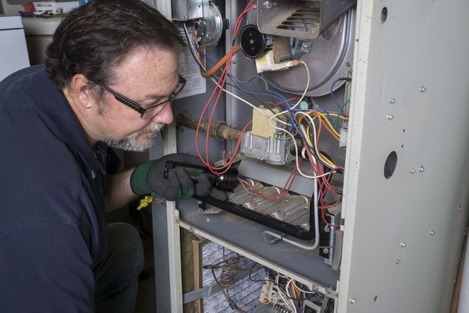 Man in glasses examining furnace components with a tool.