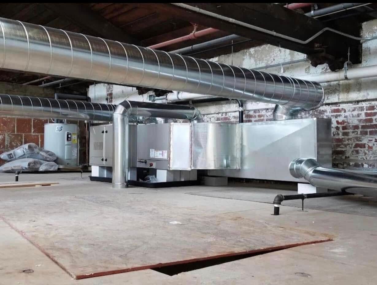 HVAC system in a basement setting with ductwork, water heater, and exposed brick walls.