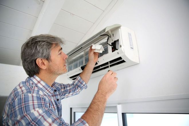 Man repairs a wall-mounted air conditioning unit with a screwdriver, indoors.