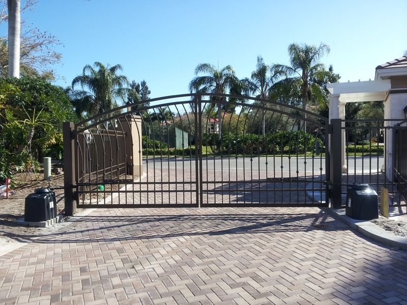 A brick driveway with a gate and palm trees in the background