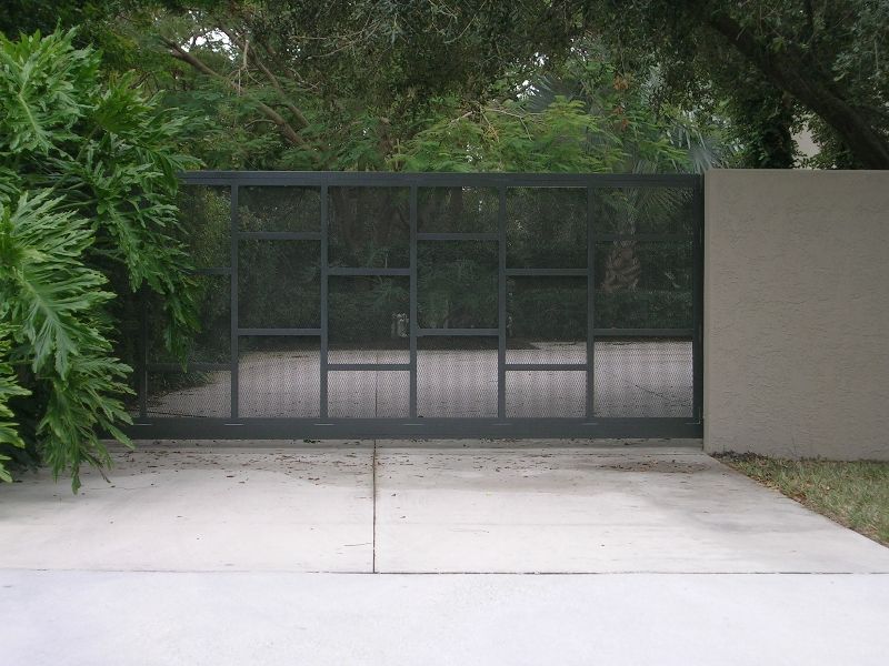 A sliding gate is open to a driveway with trees in the background