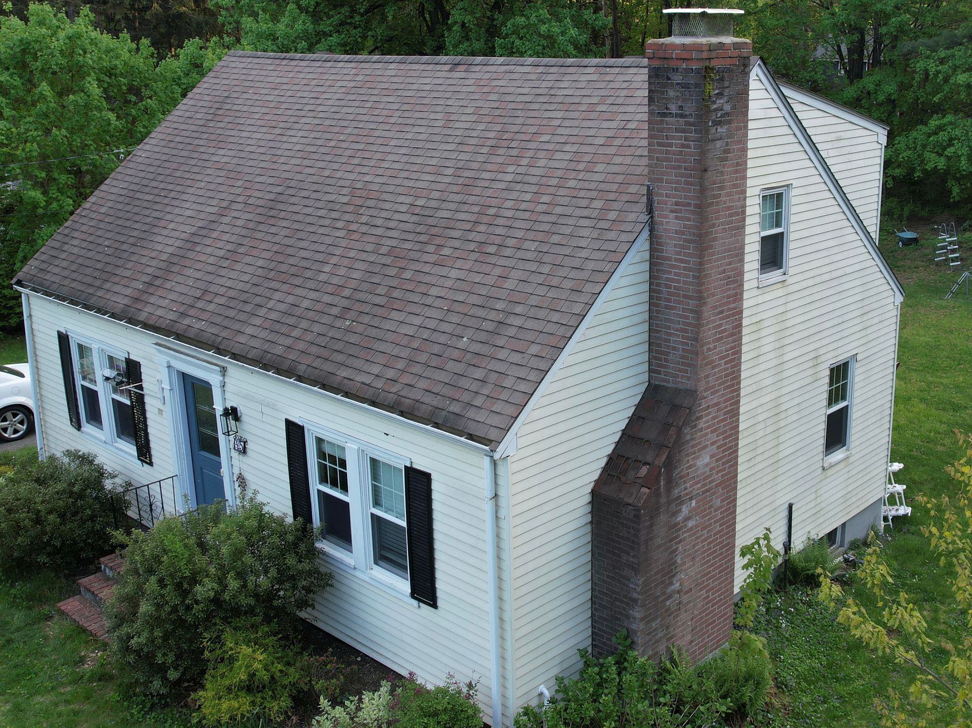 An aerial view of a white house with a brown roof and a chimney.