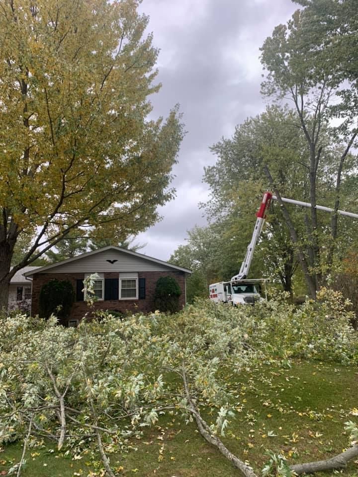 A bucket truck parked in a yard with scattered fallen tree branches in front of a residential house.