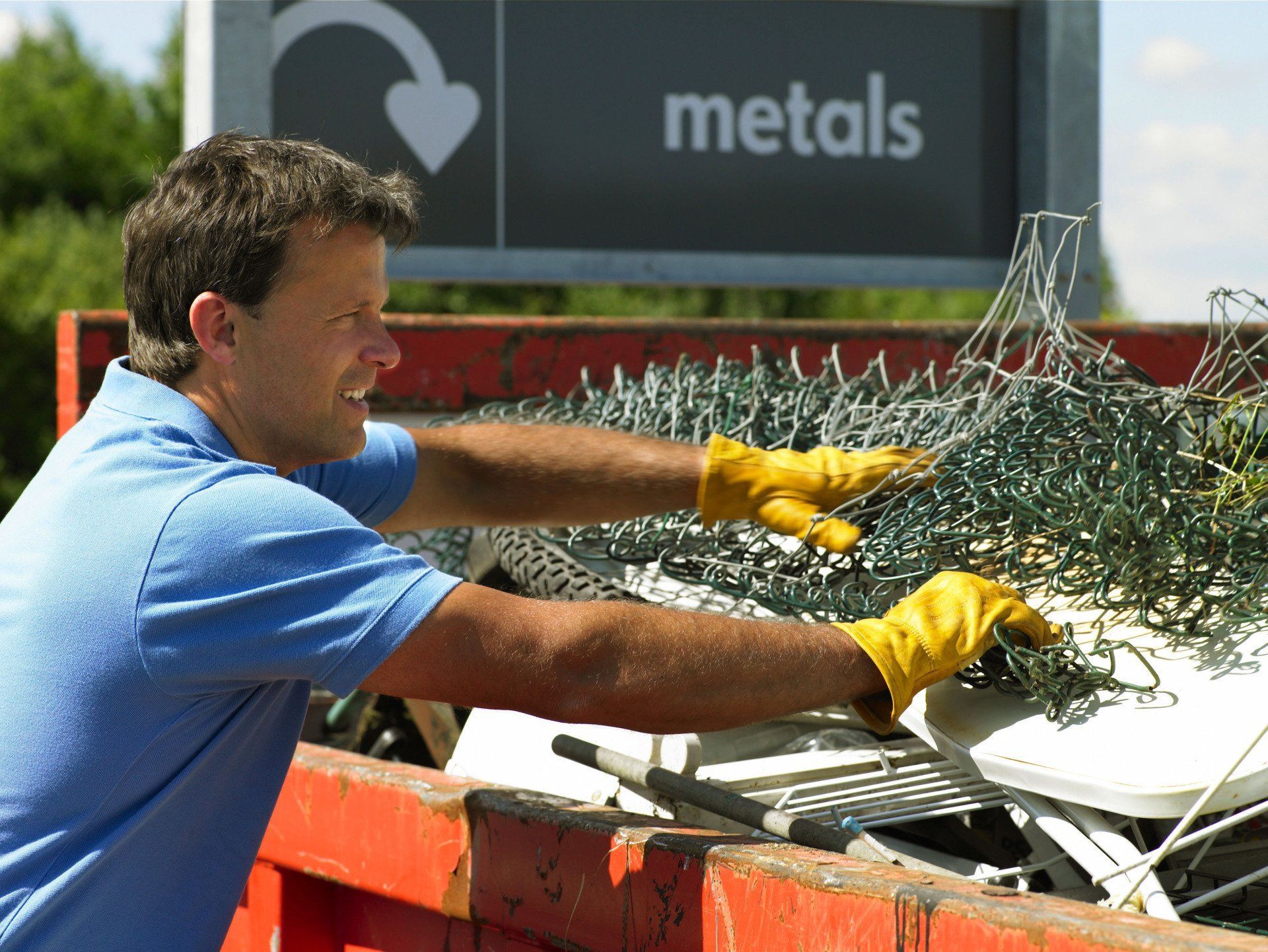Man in blue shirt, yellow gloves sorting metal recycling.