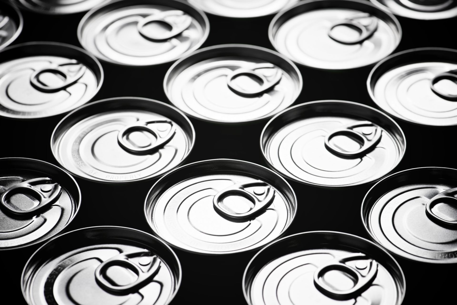 Overhead view of several metal food cans, each with a pull tab, arranged on a dark surface.