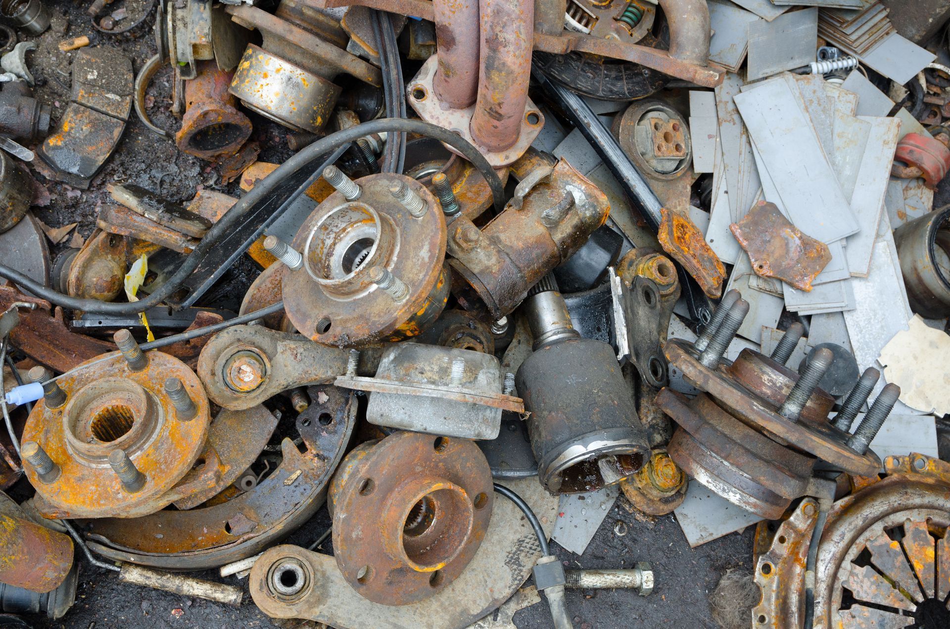 Pile of rusted automotive parts including hubs, brake rotors, and exhaust components.