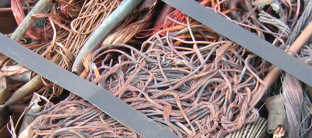 Pile of tangled copper wires, various colors, behind a diagonal metal bar.