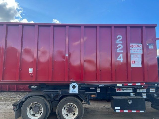 Red dumpster on a trailer with the number 224, parked against a blue sky.