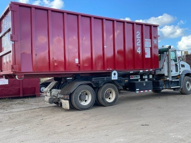 Red dumpster on a trailer truck; parked outside on a sunny day.