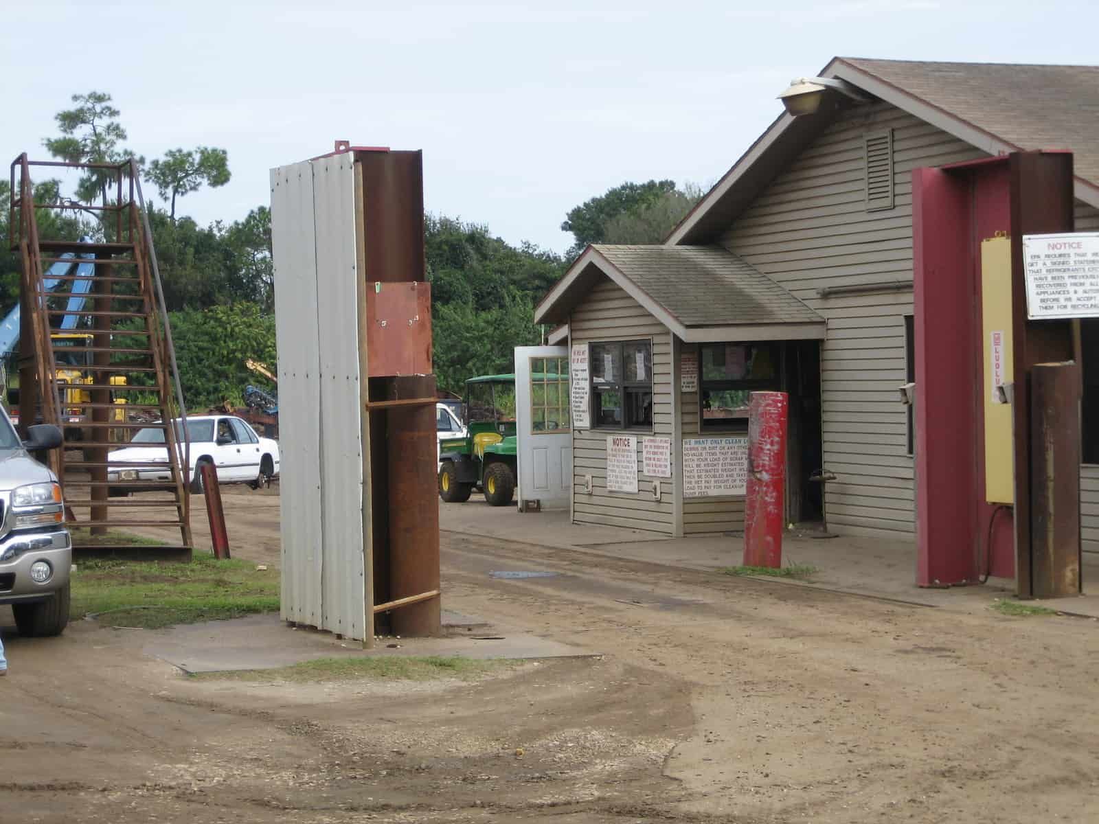 Entrance to a business with gate posts, a small building, and vehicles on a dirt road.