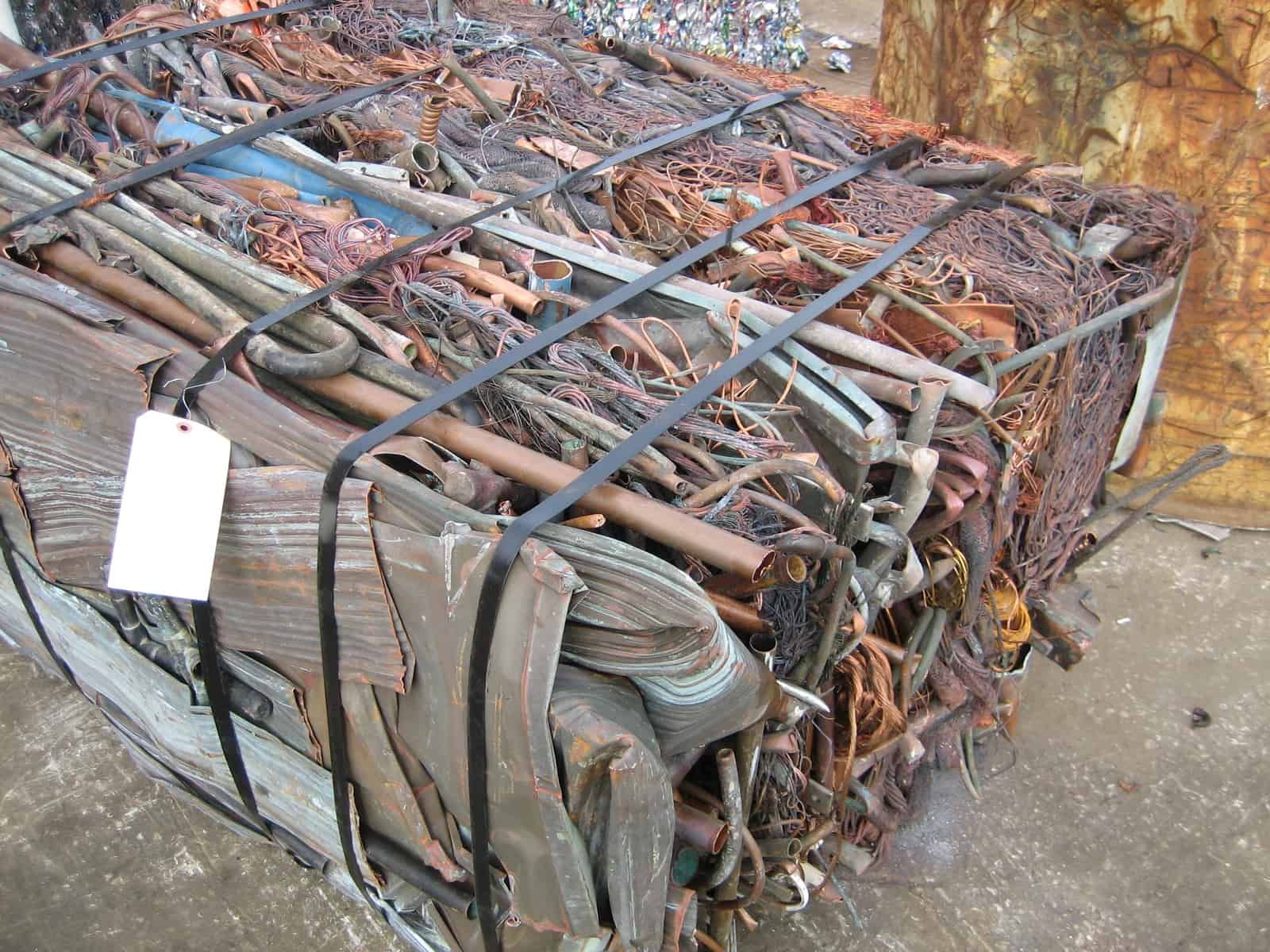 Baled scrap metal, including copper tubing and wires, bound with black straps, with a white tag.