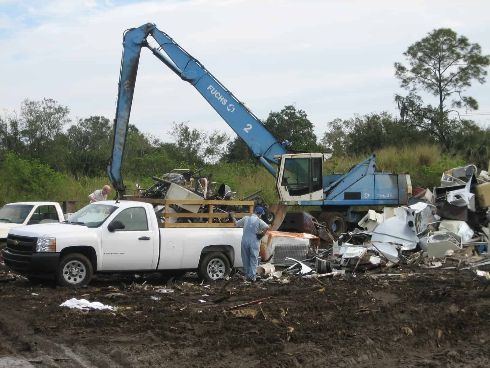 A large blue machine sorting metal scraps at a recycling center with a white pickup truck.