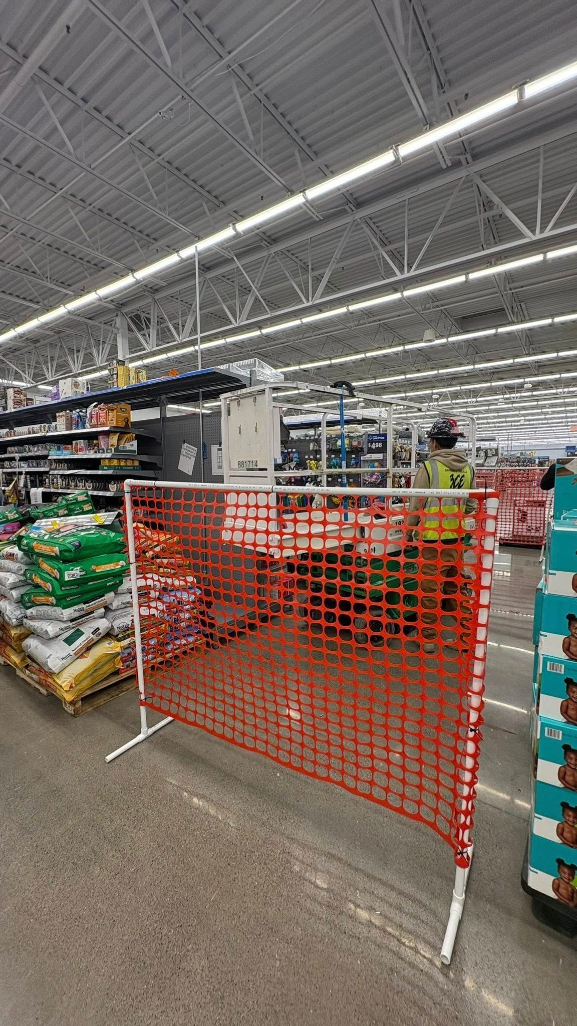 Red safety barrier in a store aisle. Pallets of goods and overhead lights in the background.