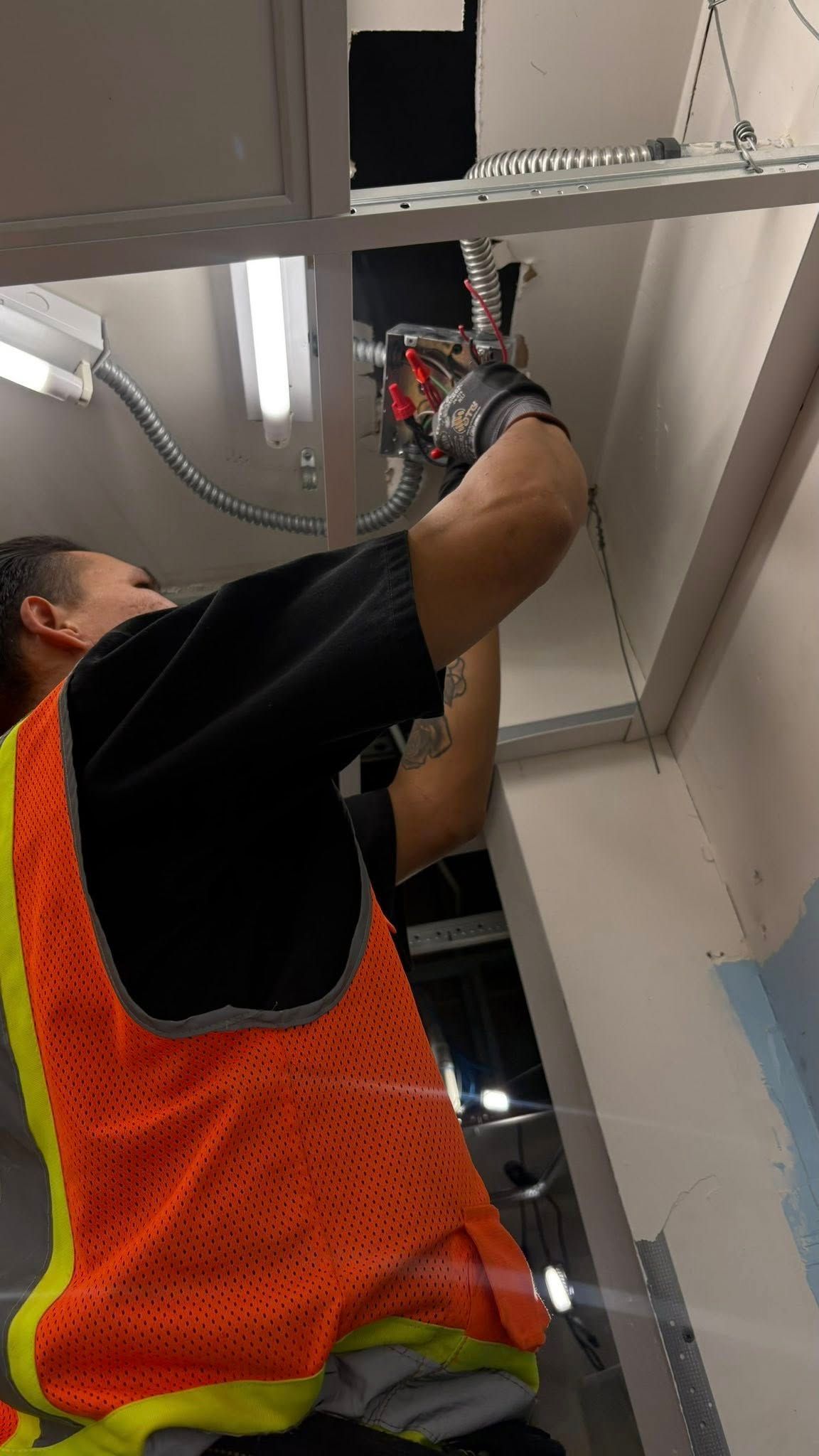 Person in safety vest using a tool on a ceiling structure.