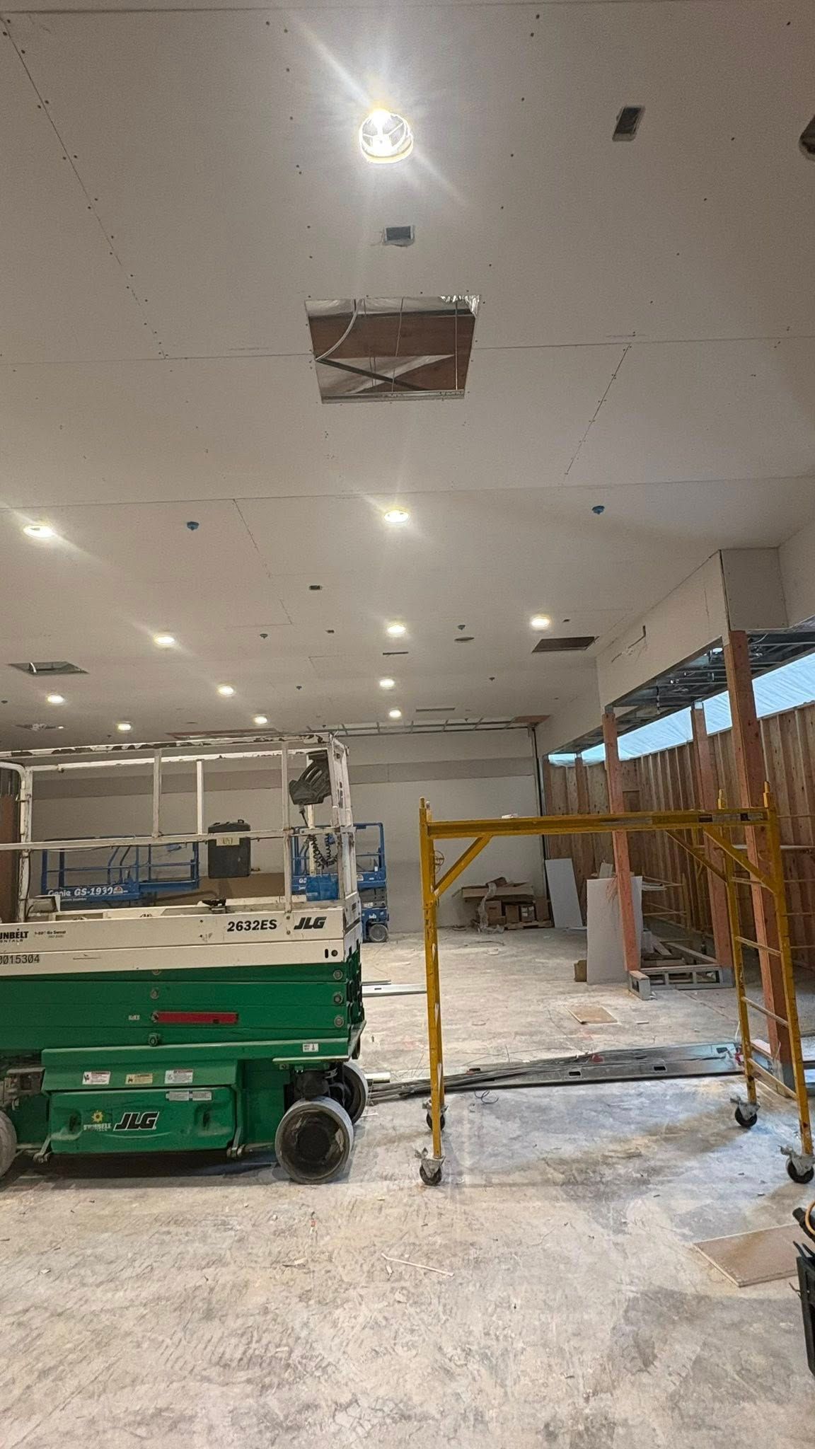 Interior construction site with lift, scaffolding, exposed ceiling, and dim lighting.