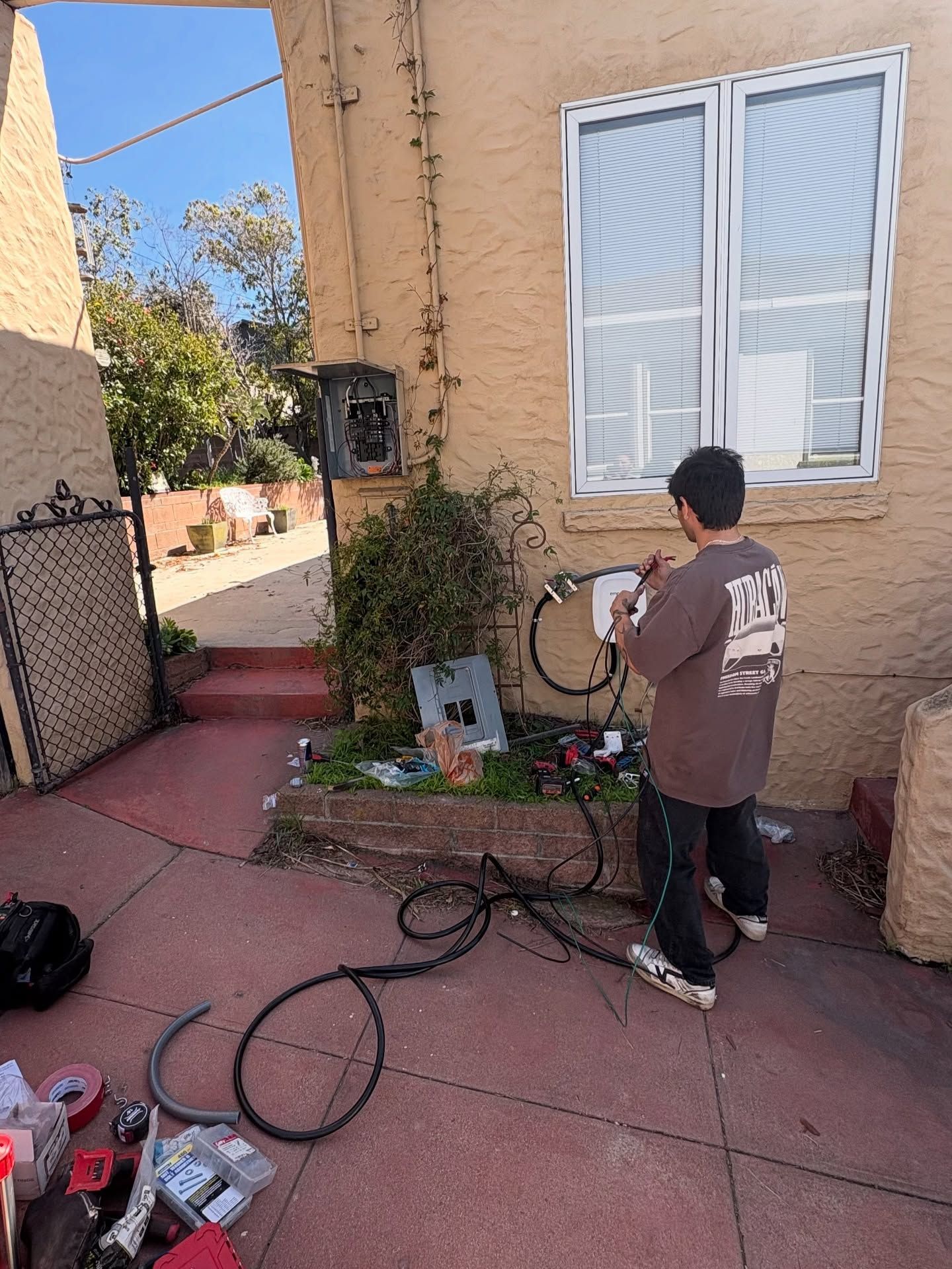 Person working on electrical equipment in a courtyard next to a building with a window.