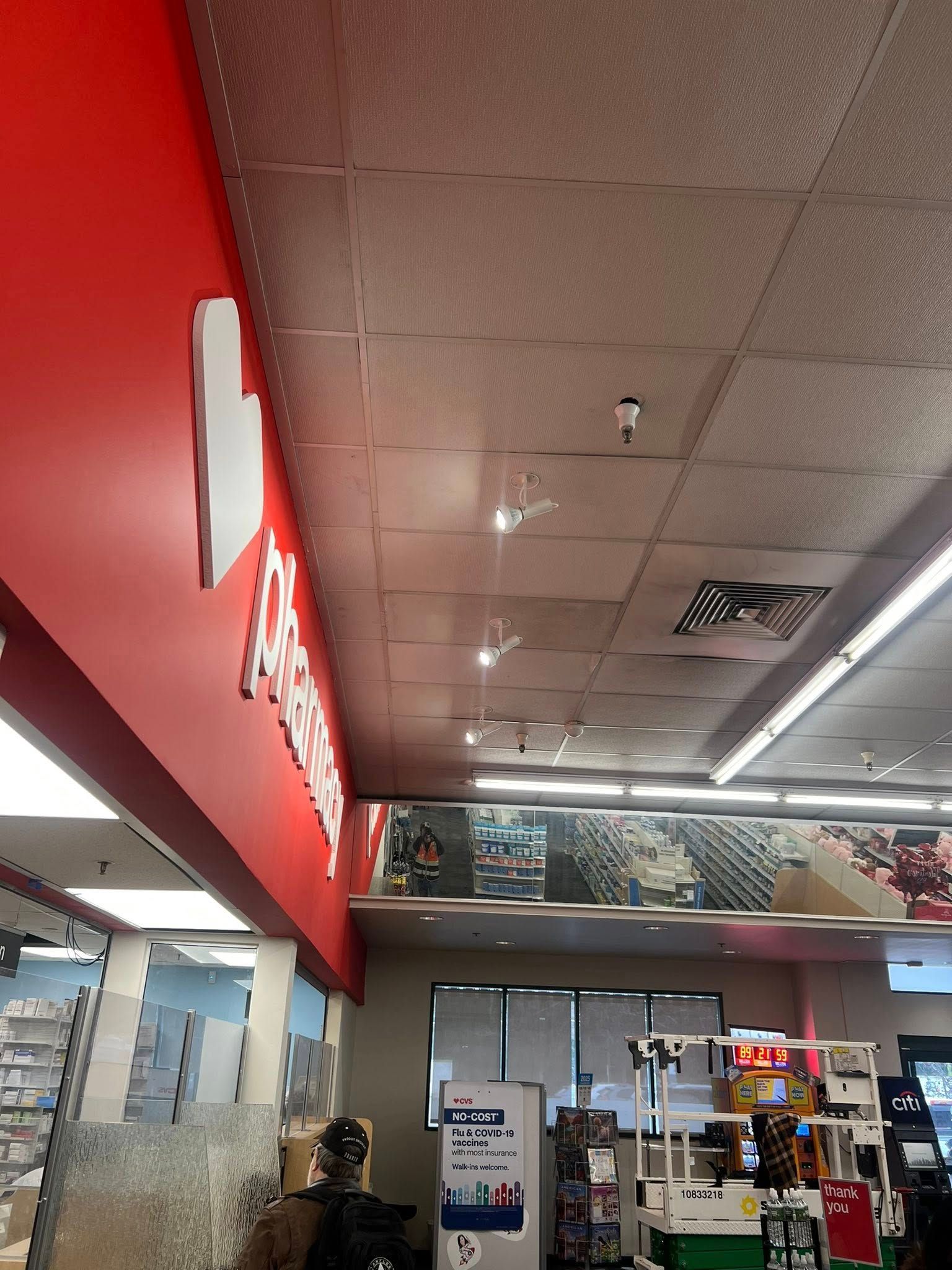 Pharmacy interior with red wall, white sign, and a view of ceiling lights and products.