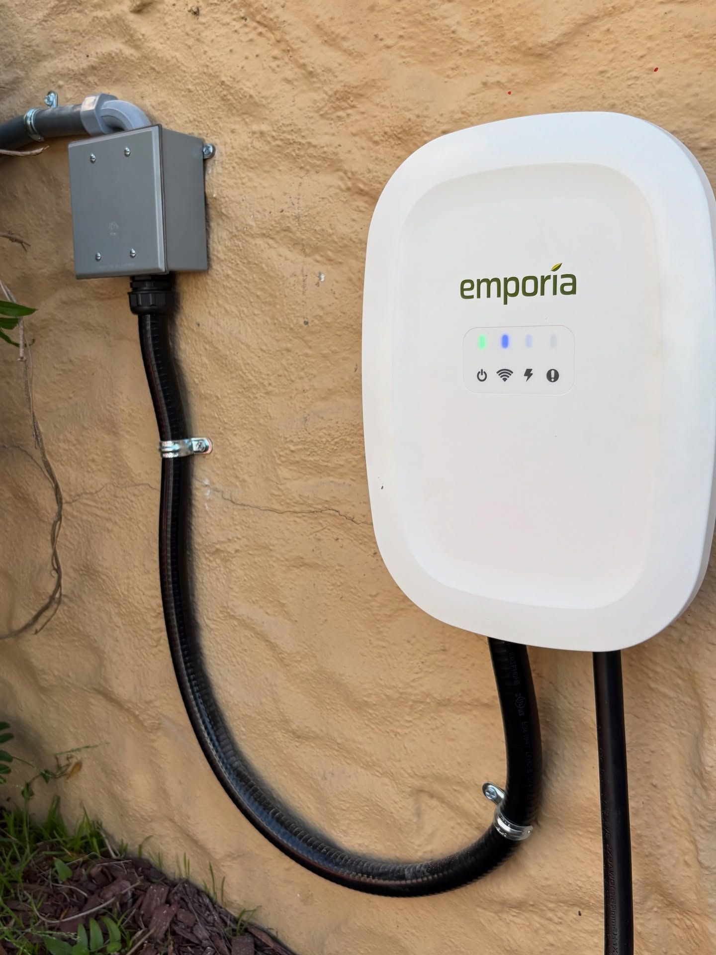 White Emporia EV charger mounted on a textured tan wall, connected to a gray electrical box.
