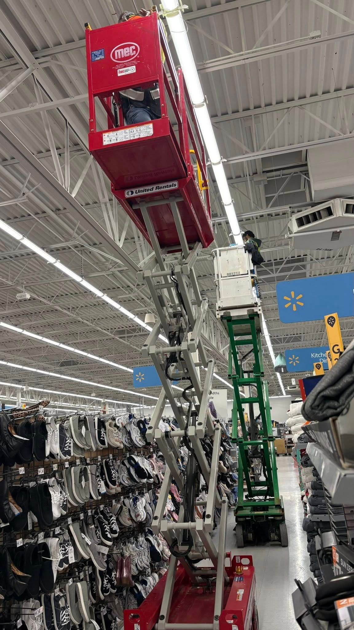 Two scissor lifts in a store, one red and one green, reaching toward the ceiling.