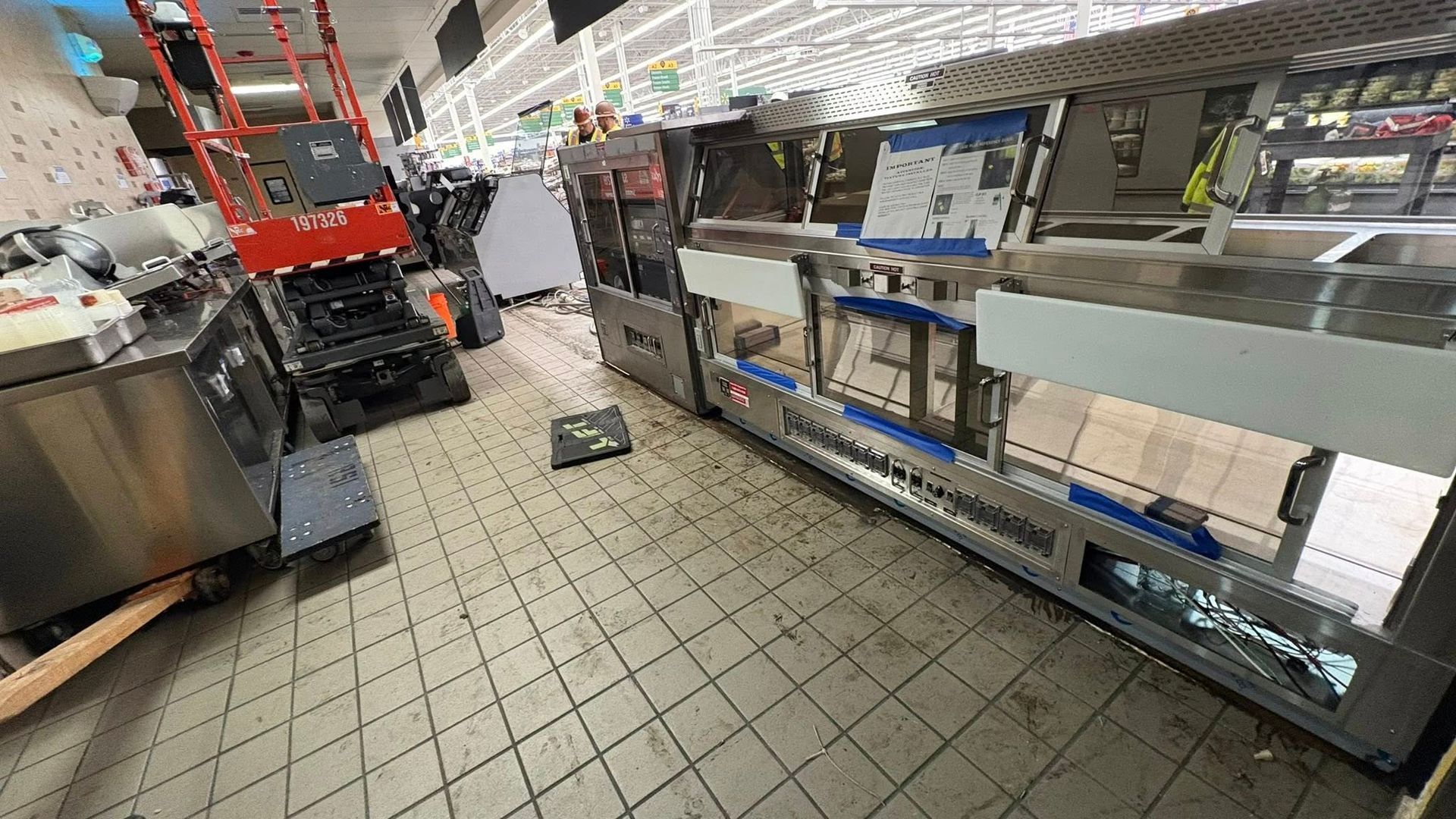 A commercial kitchen with stainless steel equipment, a red lift, and tiled floor, possibly under construction.