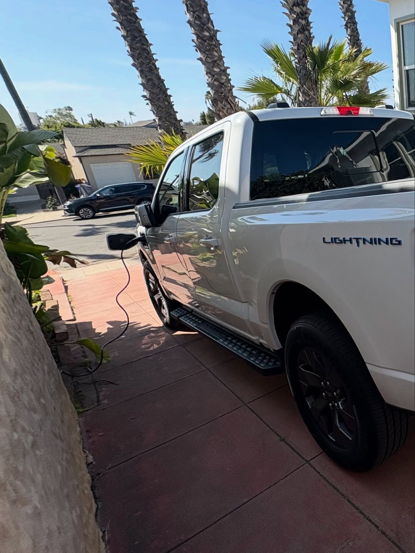 White Ford Lightning pickup truck parked on a driveway, charging cable visible.