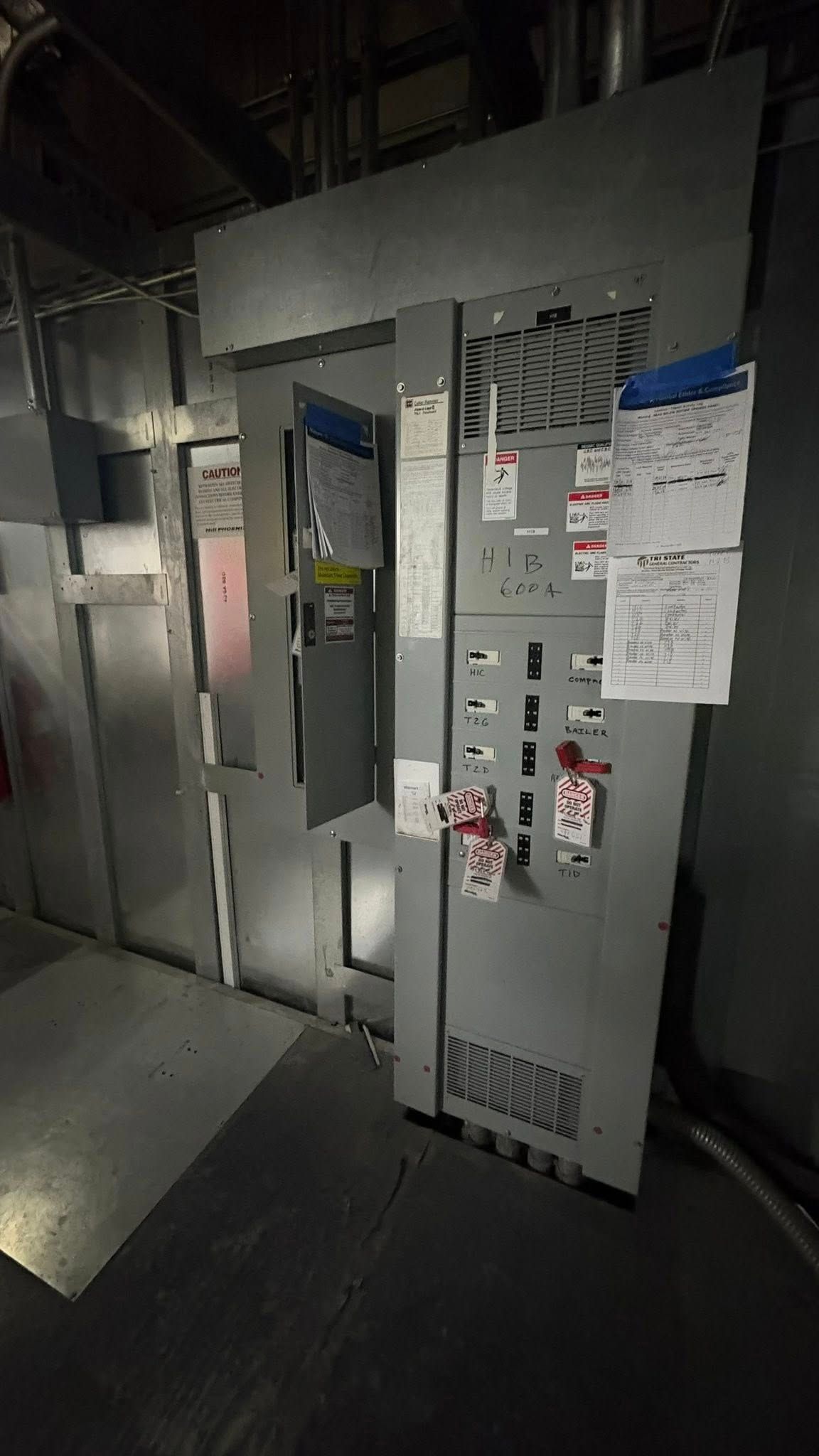 Electrical panel with open door, various gauges, and warning labels in an industrial setting.