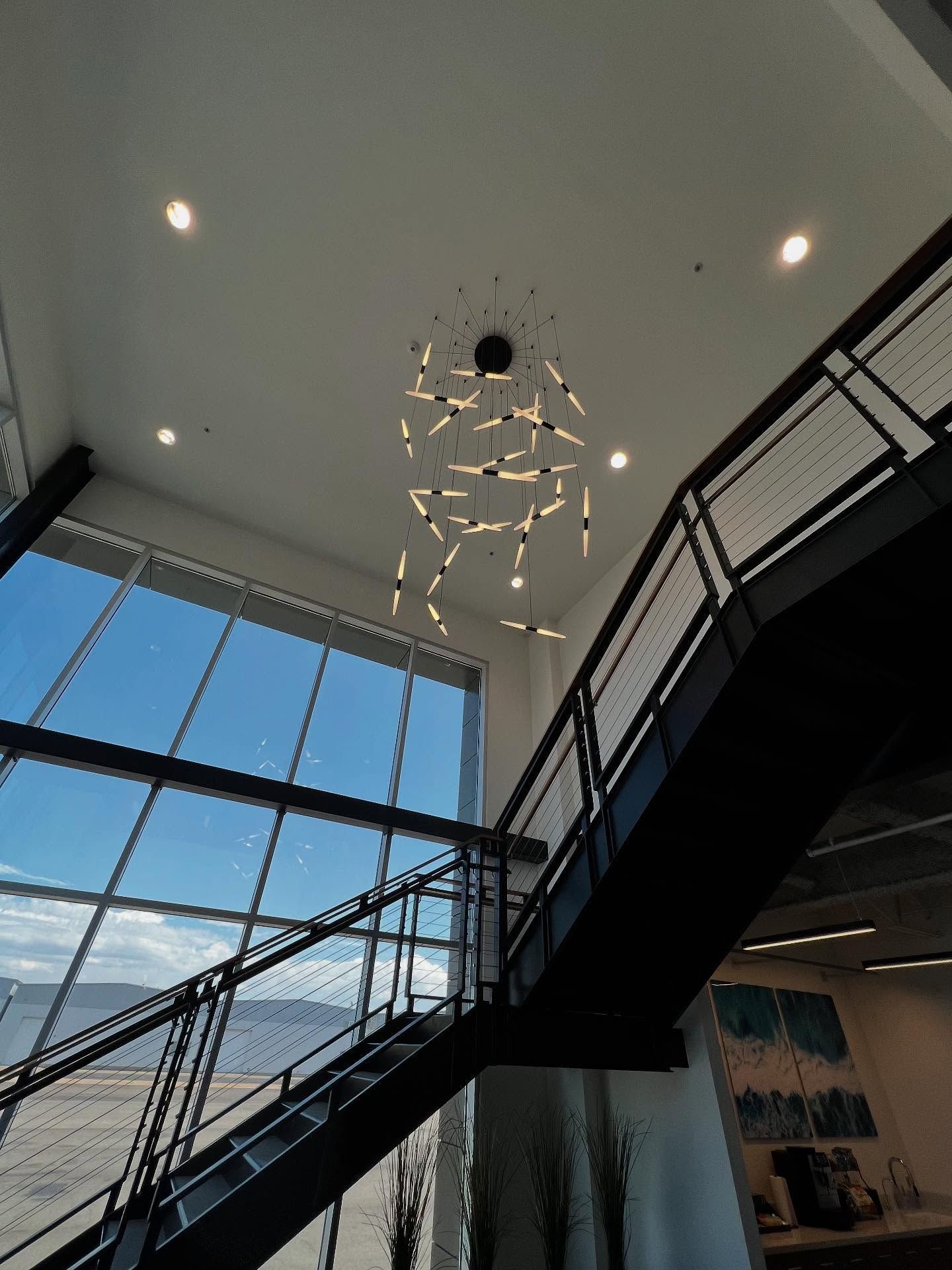 Staircase with black railing and large window, modern chandelier hangs from ceiling.