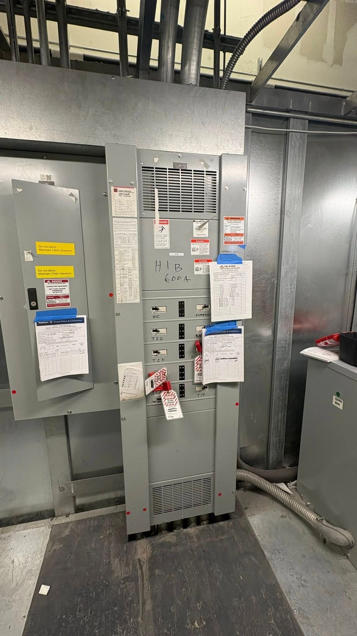 Electrical panel in a gray metal enclosure with circuit breakers and attached labels and tags.