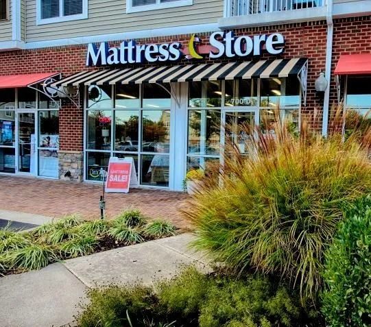 Mattress Store storefront with awning and sale sign. Brick building, landscaping in front.