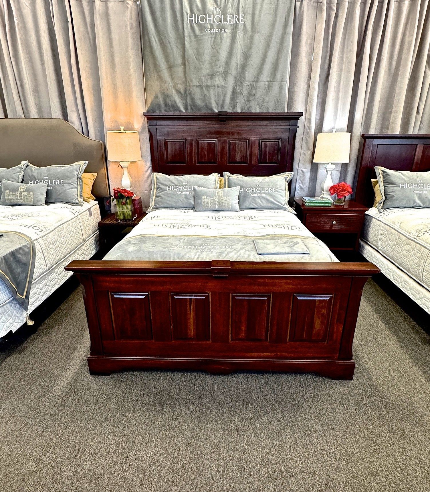 Wooden bed frame with headboard, nightstands, and bedding in a showroom setting.