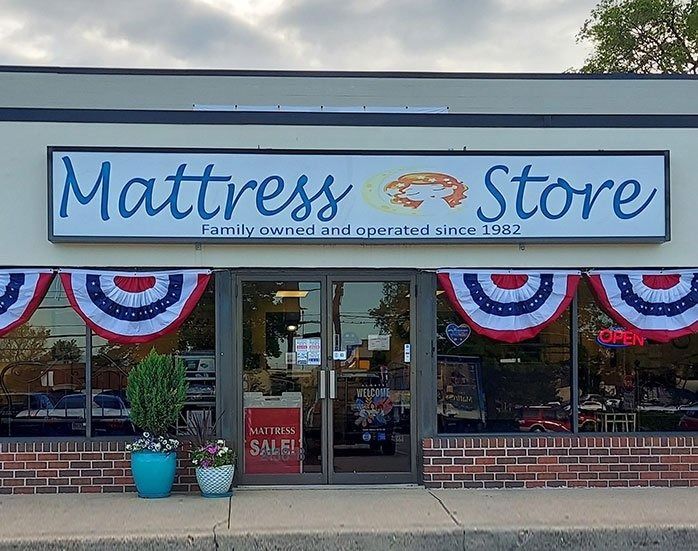 Mattress Store storefront with sign, red, white, and blue bunting, brick facade, and glass door.