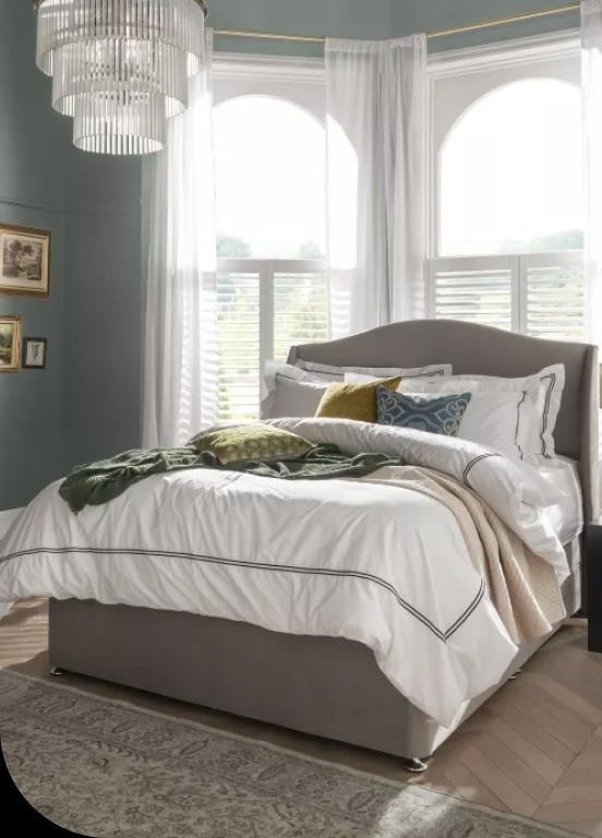 Bedroom with a gray bed, white bedding, and large arched windows with sheer curtains.
