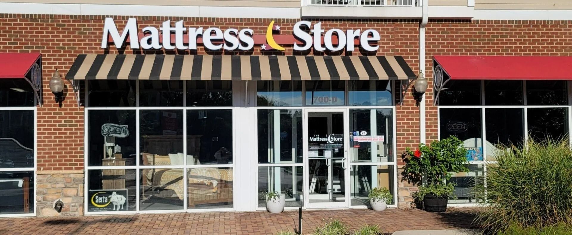 The Mattress Store storefront, with sign, awning, and large windows. Red awnings flank the sides of the building.