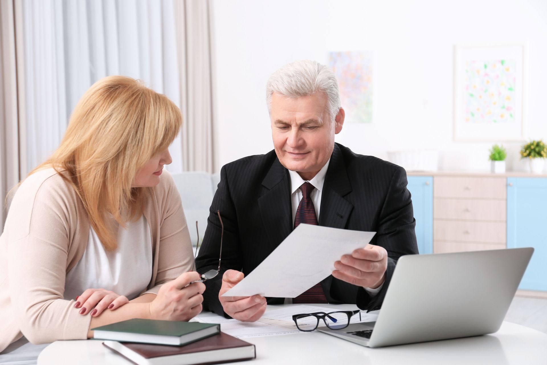 Two people reviewing documents at a desk with a laptop in a bright office