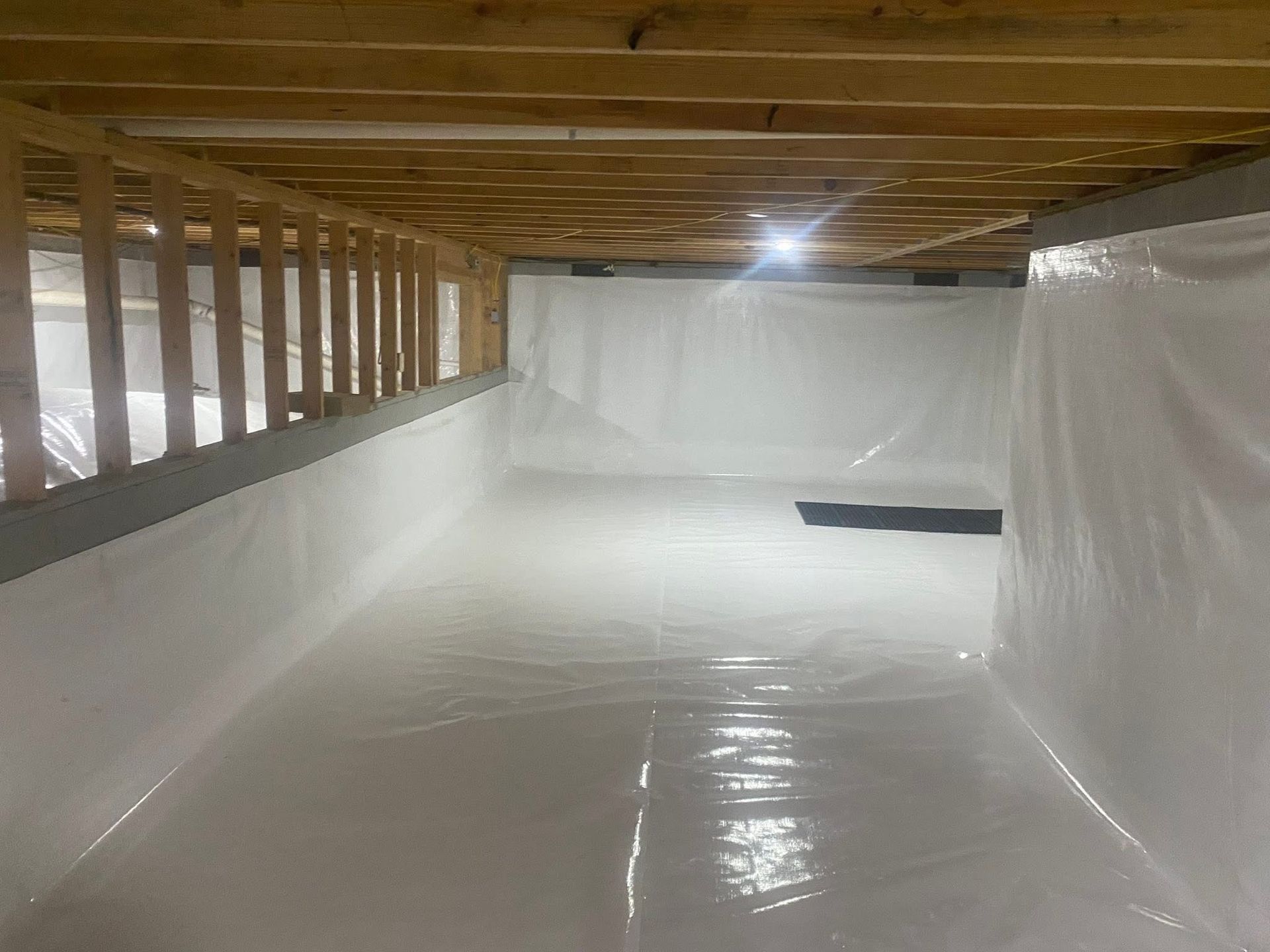Crawl space covered in white plastic sheeting. Wooden supports and beams overhead, creating a clean, moisture-controlled environment.