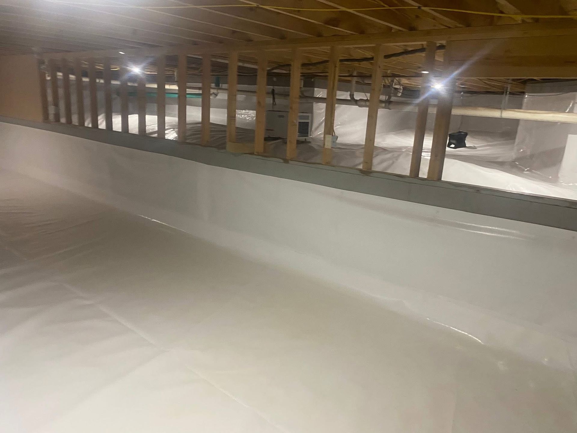 White crawlspace with vapor barrier and exposed wooden joists.