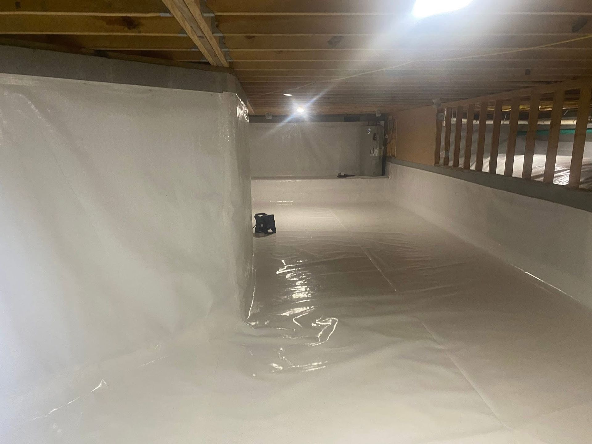 Basement with white wall lining and flooring, lit by overhead lights, looking clean and newly renovated.