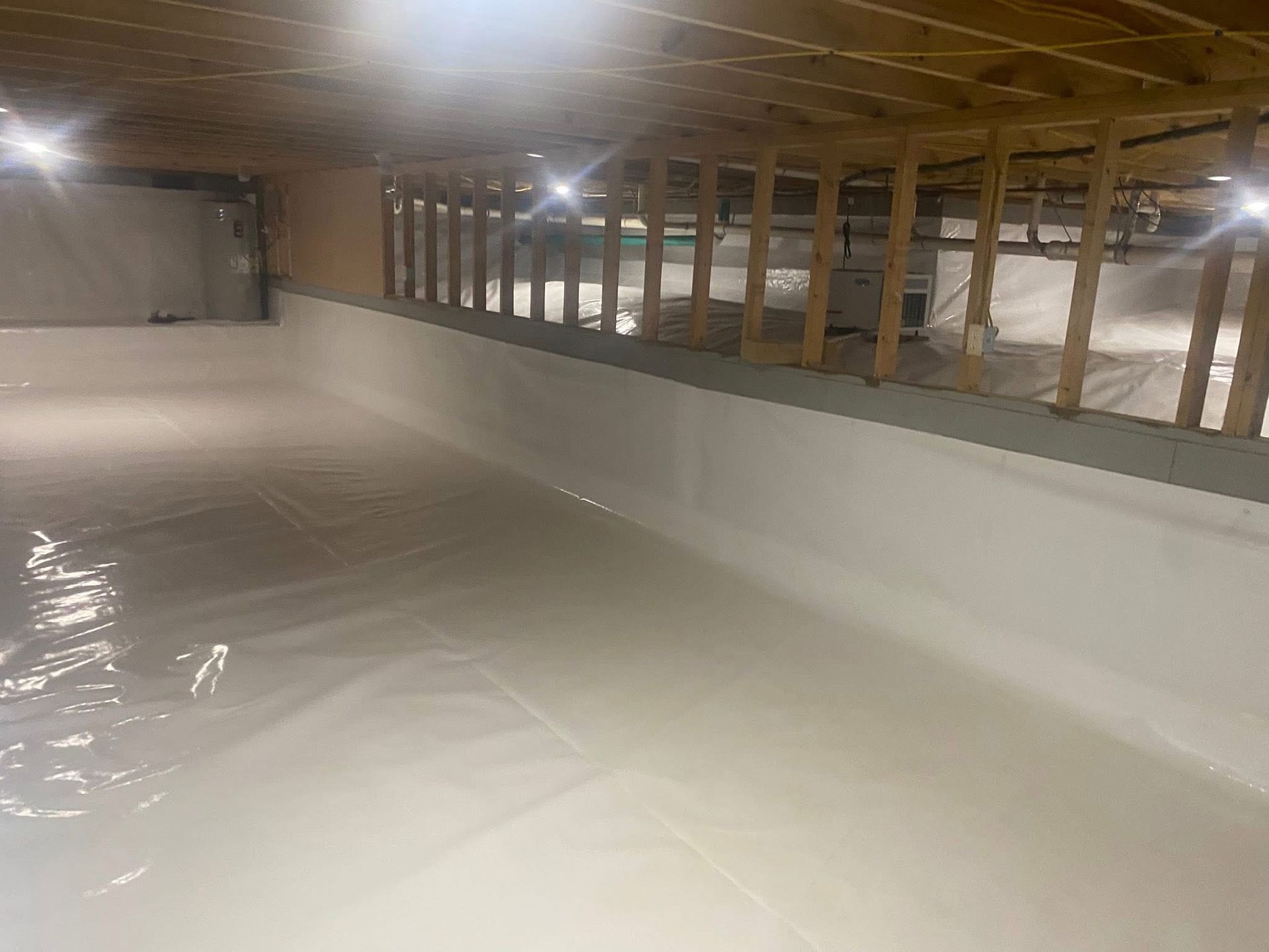 White crawl space with plastic sheeting on floor and walls, wooden beams overhead.