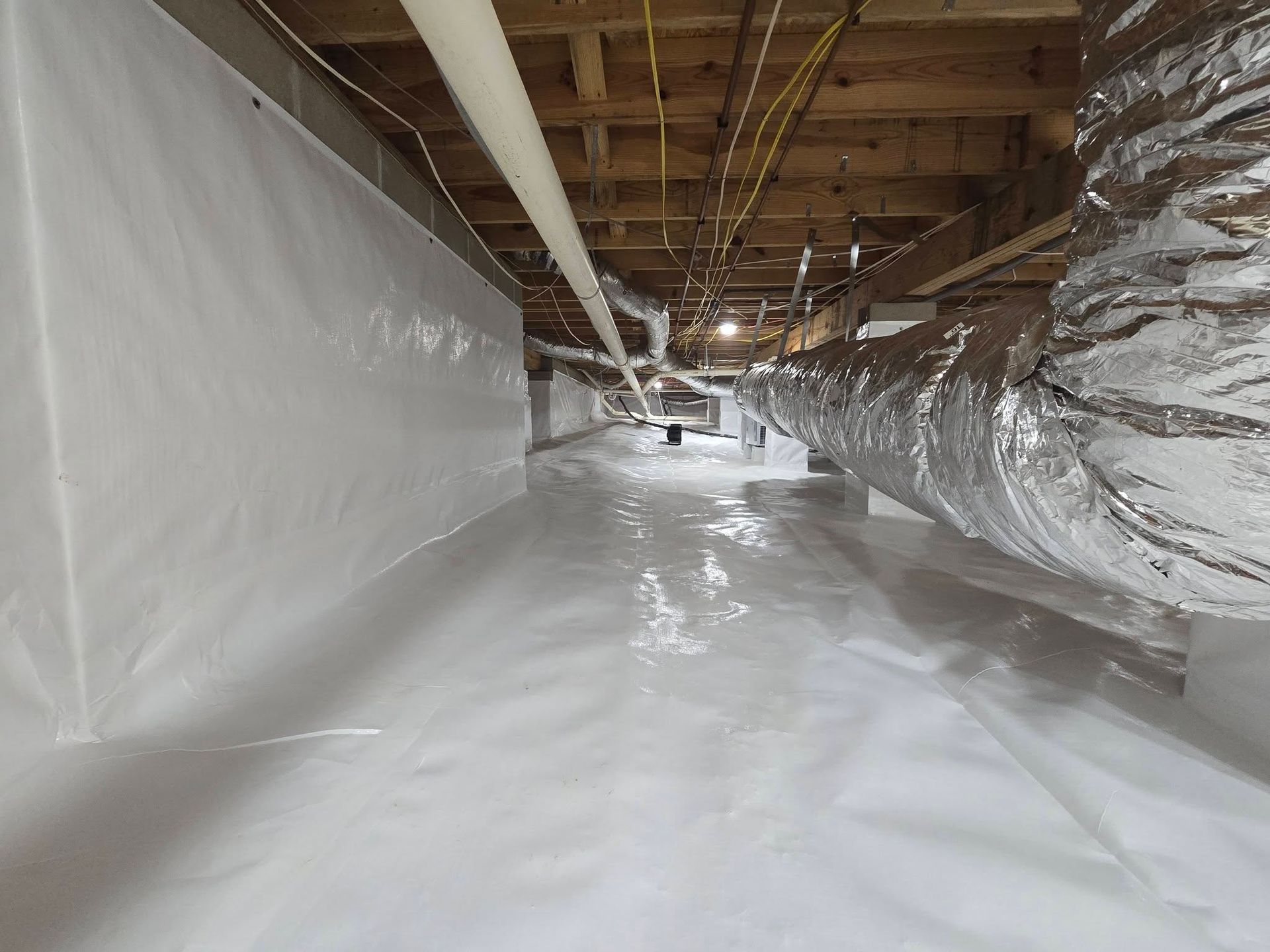 Plastic-lined crawlspace with exposed pipes and wooden joists, covered in white sheeting