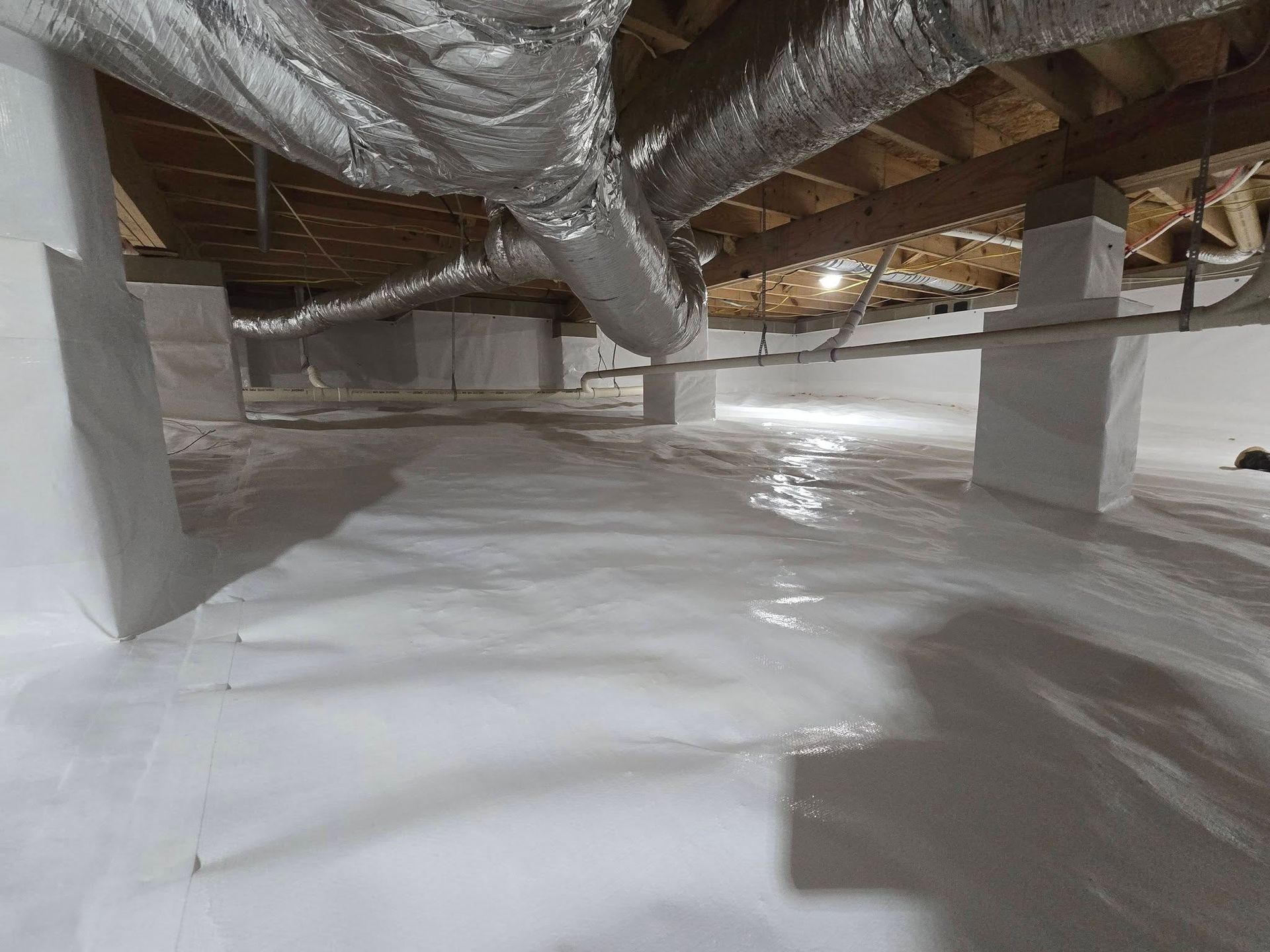 Crawlspace with white vapor barrier, exposed ductwork, and insulation under the floor