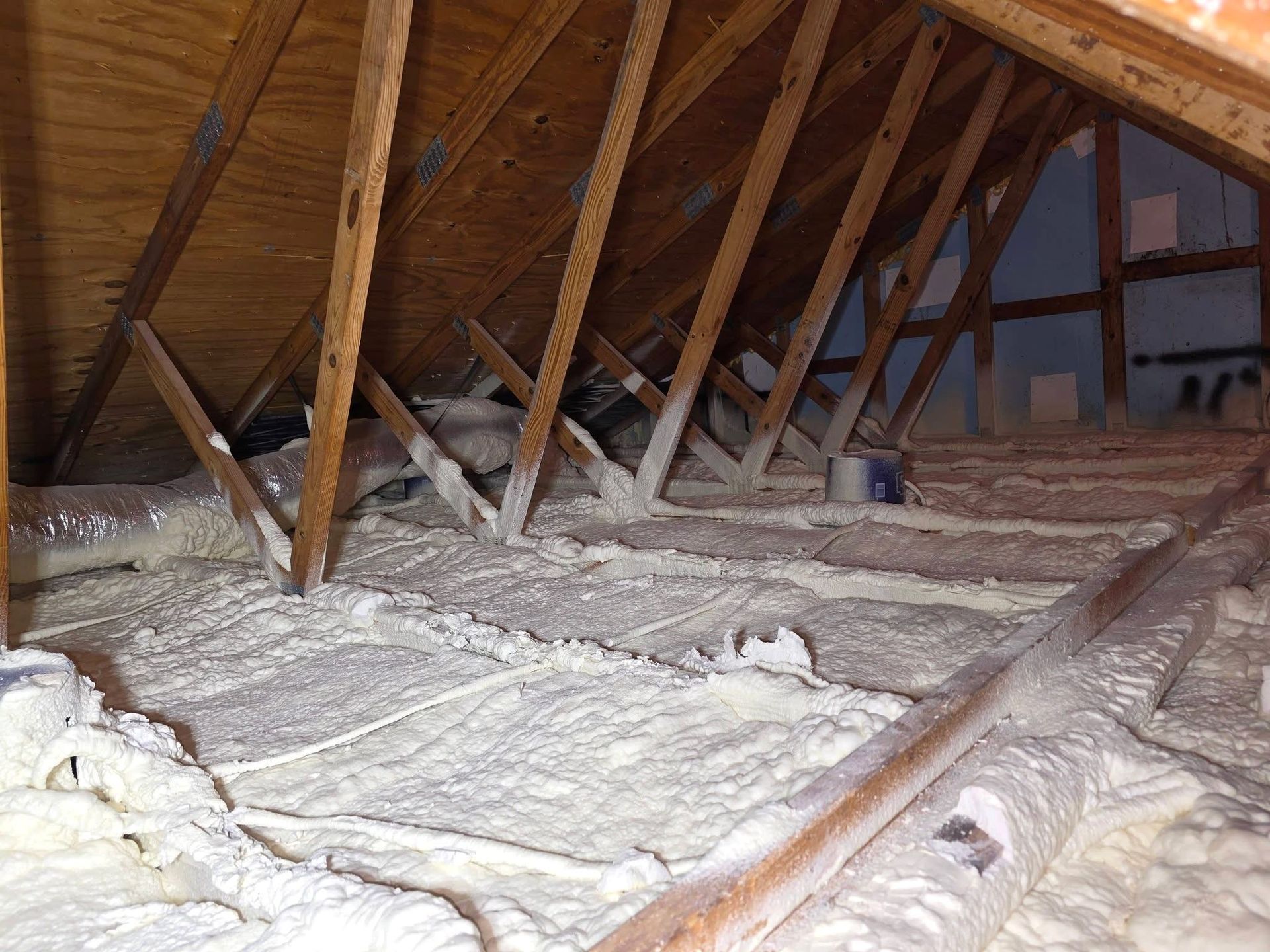 Attic space with spray foam insulation on the floor and rafters; wooden beams, ductwork, and wiring are visible.