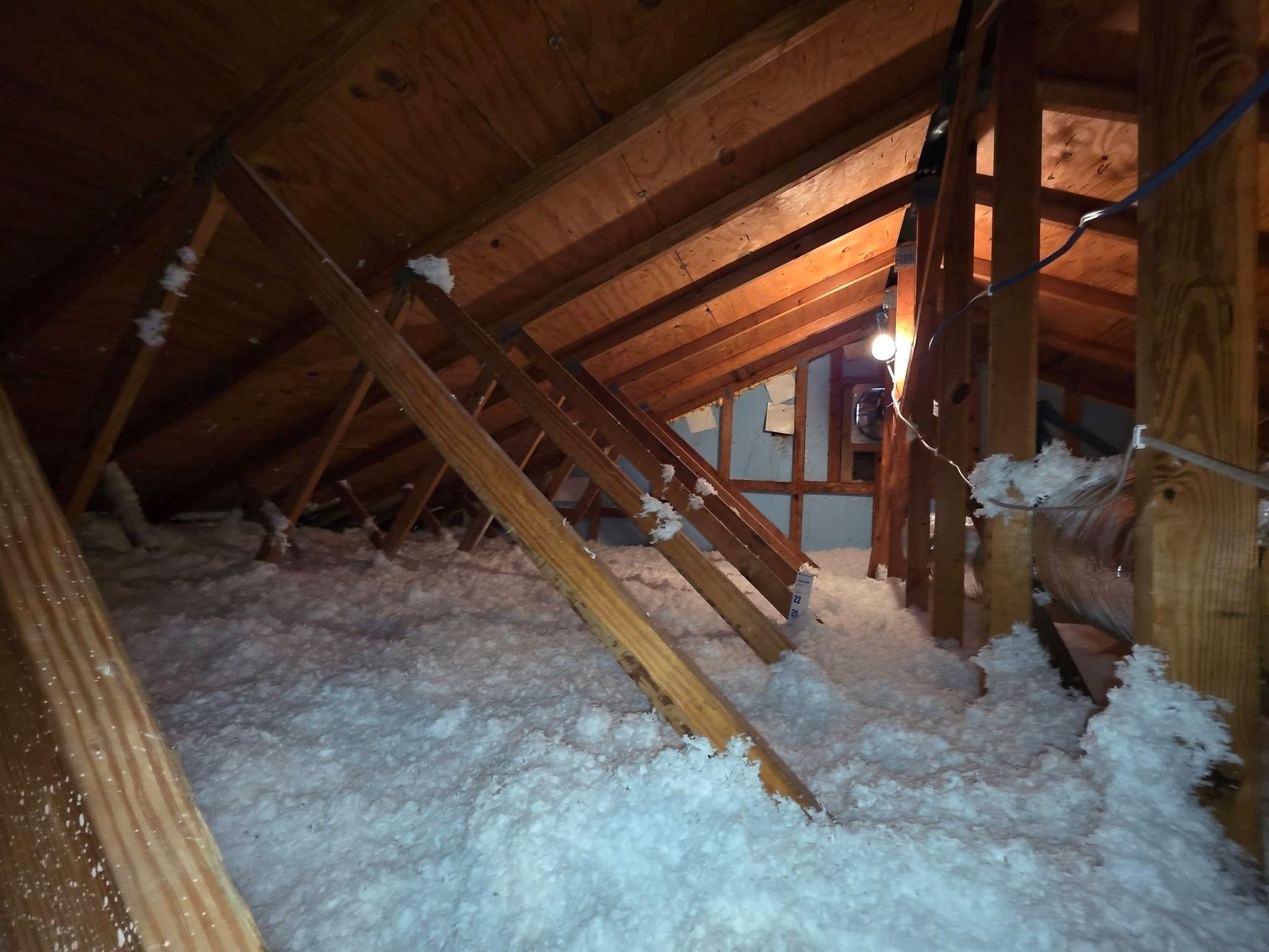 Attic interior with wooden beams and white insulation covering the floor.