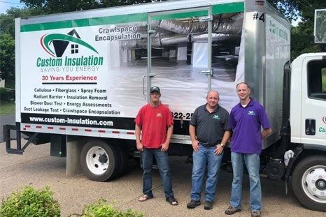 Three men pose in front of a Custom Insulation truck. The truck is white and green with company branding.